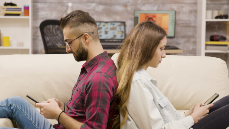 terapia par online. para siedzi do siebie tyłem na kanapie, oboje patrzą w telefony. Zdjęcie ilustruje brak komunikacji i oddalenie w związku.